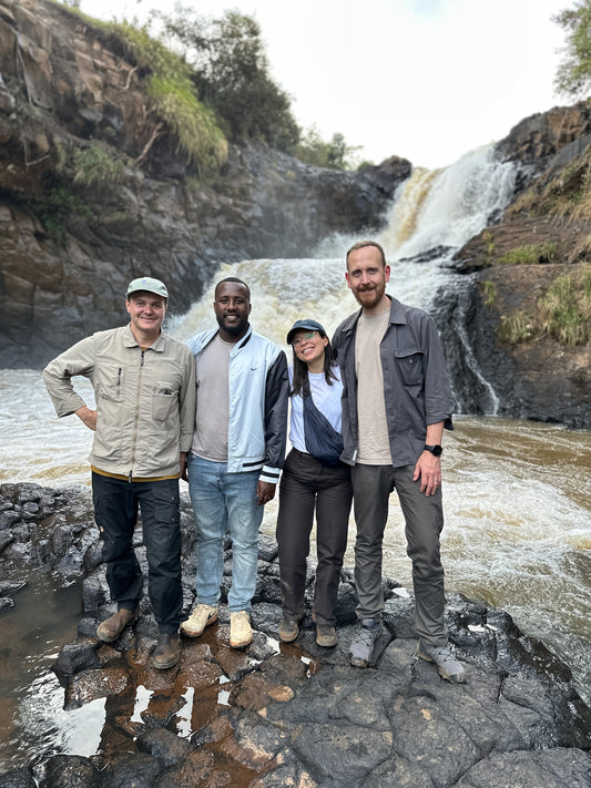 Four people posing for a photo in front of a waterfall.