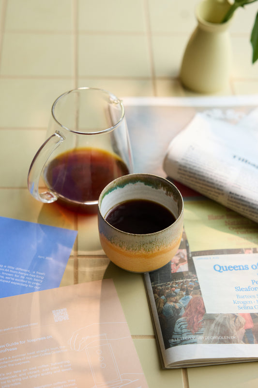 Coffee cup and glass mug on a tiled surface with a magazine underneath