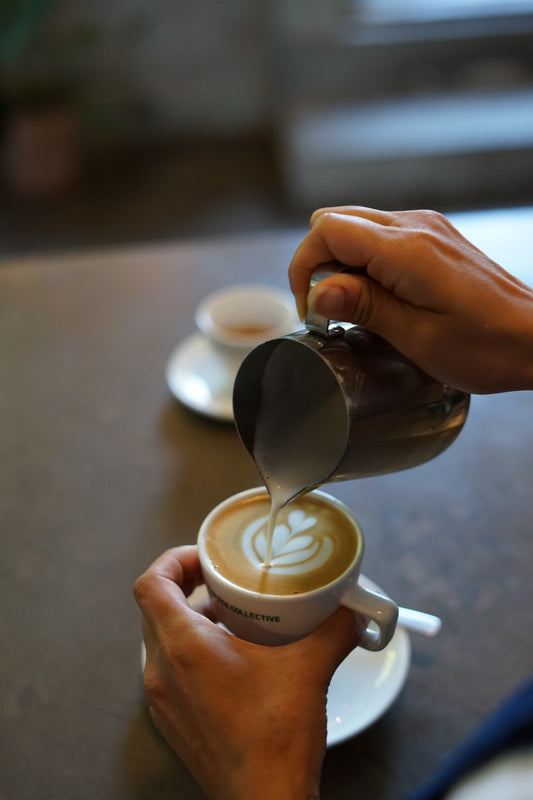 Person pouring milk into a cup of coffee with latte art.